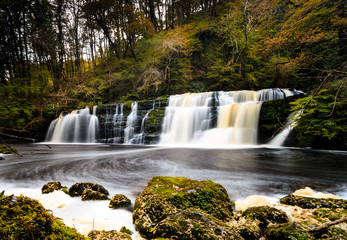Long exposure of a waterfall (Sgwd Y Pannwr) in a tree covered forest in the autumn