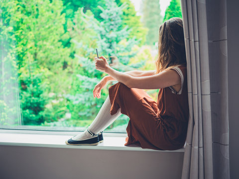Young woman sitting by the window with phone