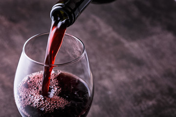 Rotwein in das Glas vor Holzhintergrund gießen