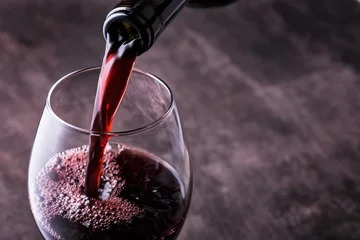 Foto auf Acrylglas Wein Rotwein in das Glas vor Holzhintergrund gießen