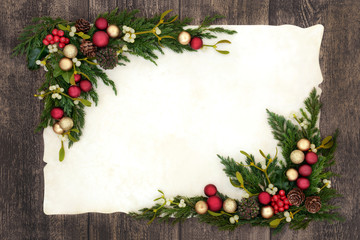 Christmas background  border on parchment paper on oak wood with red and gold bauble decorations, holly, mistletoe, ivy, fir and pine cones.