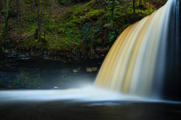 Long exposure of a waterfall in full flow in a forested gorge