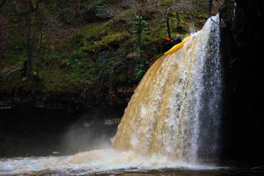 A canoe being paddled off a tall, fast flowing waterfall