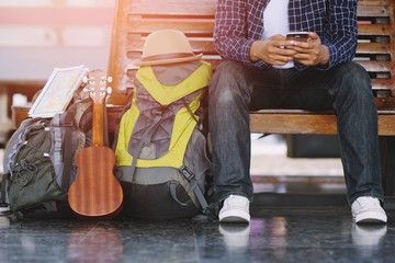 Fototapeta na wymiar Young man traveler with backpack and Travel equipment sit use phone with waiting for train. Travel concept.