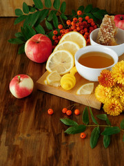 Liquid honey in a little bowl surrounded by slices of lemon, apples, rowan berries and flowers on a wooden board