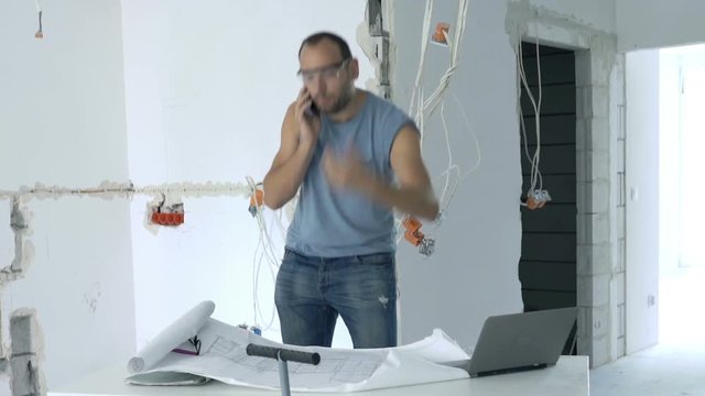Angry male worker talking on cellphone standing at new home
