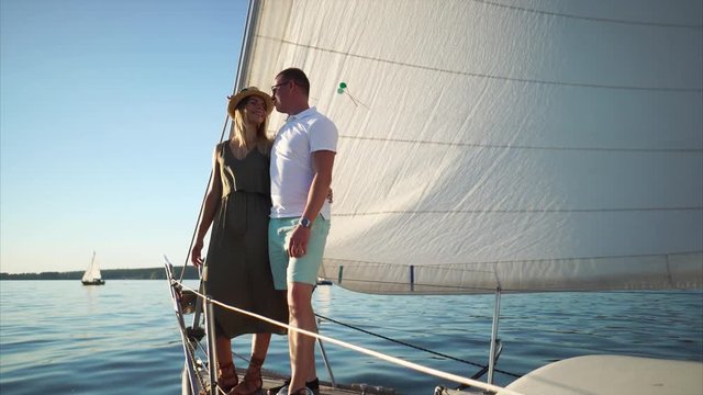 Young loving couple standing on the front deck of sailboat. Romantic date on the yacht