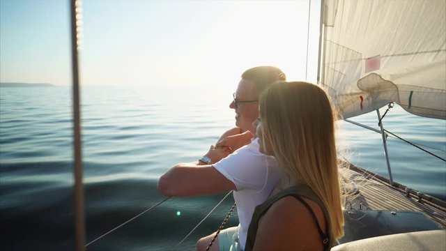Couple in love is riding on the yacht in sunny summer day. Woman is embracing her man, speaking and enjoying of nature in no windy weather.