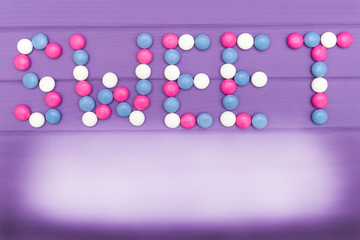 Image of word Sweet made of colorful candies on violet background