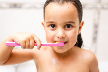 little child is brushing her teeth in bath