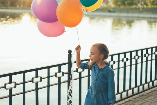Cheerful girl holding colorful balloons and childish suitcase wa
