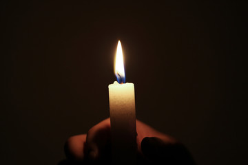 holding a burning candle in darkness 