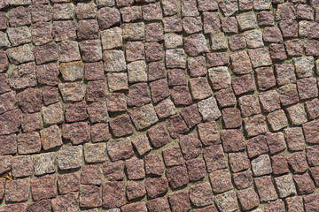 Square lined with cobblestone or stone pavement, walkway or road. The surface of rough stones and rough. Stones brown. Seams of sand. The cobbles have a mottled pattern and texture.