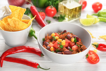 Chili con carne in bowl served with chips on kitchen table