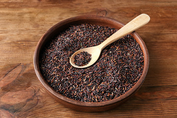 Plate with raw wild rice and spoon on wooden background