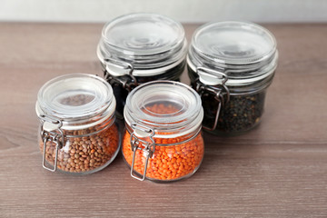 Different types of lentils in glass jars on wooden table