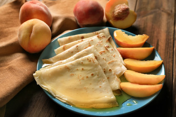 Plate of tasty thin pancakes with peaches on table