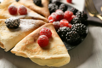 Plate with tasty thin pancakes and berries on table, closeup