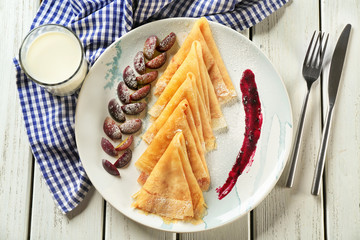 Plate with tasty thin pancakes and plums on table