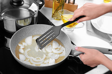 Woman frying onion in kitchen