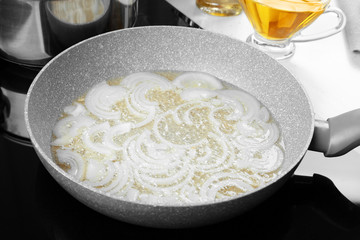 Frying pan with cut onion and oil on stove in kitchen