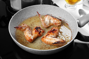 Frying pan with chicken wings and oil on stove in kitchen