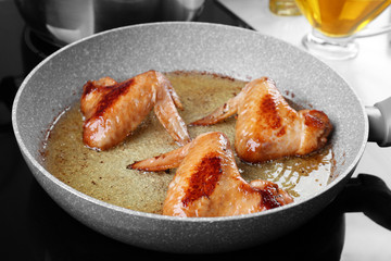 Frying pan with chicken wings and oil on stove in kitchen