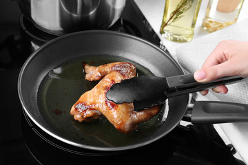 Woman frying chicken wings in kitchen