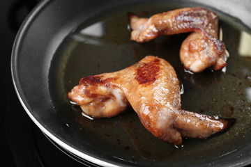 Frying pan with chicken wings and oil, closeup