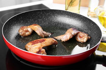 Frying pan with chicken wings and oil on stove in kitchen