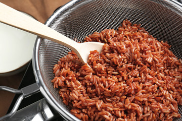 Sieve with brown rice and spoon in saucepan on stove