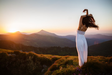 Hiker woman standing with hands up achieving the top. Girl welcomes a sun. Conceptual design. Successful woman hiker open arms on sunrise mountain top. Girl in long white dress in the mountains. - 174761536