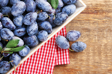 Tray with fresh ripe plums on wooden background