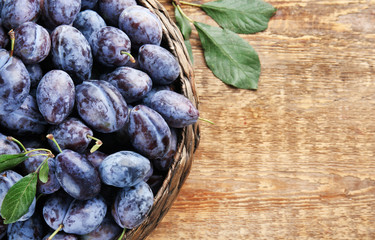 Basket with fresh ripe plums on wooden background