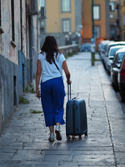 A traveling woman walking on pavement with suitcase.