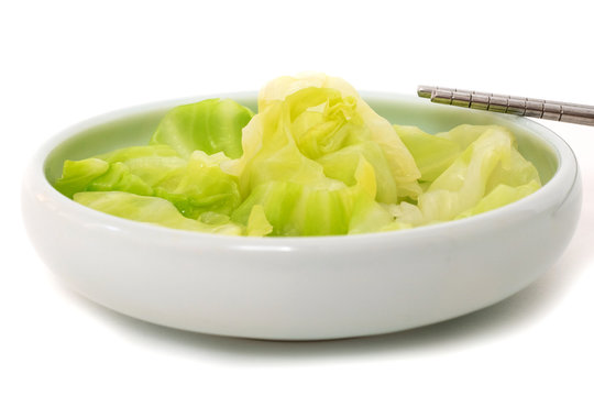 Cooked cabbage in a round shallow vegetable bowl and chopsticks aside with white background