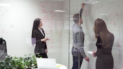 Business man writes on a white board and explains something to employees in the office, steadicam shot through glass