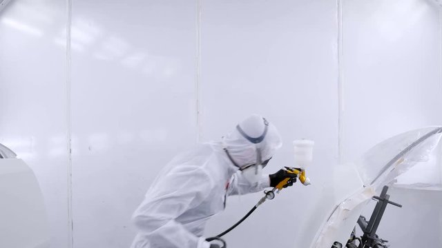A professional car painter is painting the body work of a car in a paint box of a garage with an airbrush.
