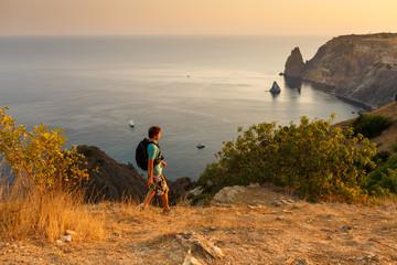 A man tourist with backpack walks along the paths near the sea on vacation on summer sunny days. In...