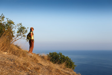 Traveling woman with backpack and hat looking at sea at sunny day. Adventure, travel people concept.