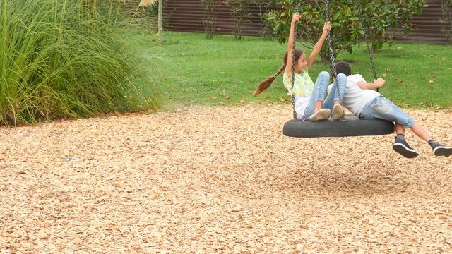 happy brother and sister swinging on a swing on the amusement park in the city. 4k, copy space, slow motion. life style