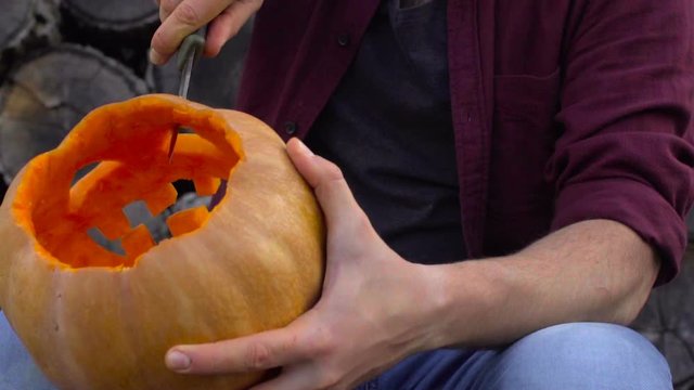 Man carves from a pumpkin Jack-o'-lantern in the backyard on a tree stump
