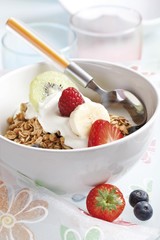 Muesli with yoghurt and fruit in a porcelain bowl, kiwi, raspberry, strawberry and blueberries