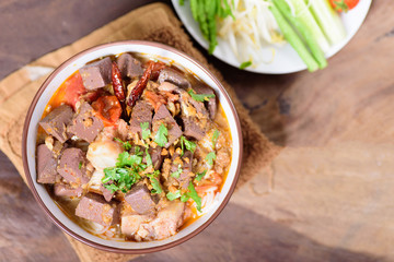 Northern Thai food (Kanom Jeen Nam Ngeaw) with vegetables on wooden background,spicy rice noodles soup,rice vermicelli served with curry.Top view of food