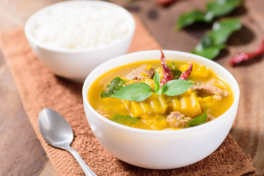 Thai food.Spicy pumpkin soup with pork and cooked rice in a bowl on brown fabric and wooden background