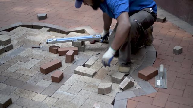 Brick paver artisan fitting a brick into the herringbone two-tone pattern and using a rubber mallet to fit it properly.