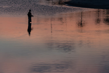 Fototapeta na wymiar Silhouette of unrecognisable fisherman in the lake on sunset