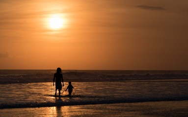 Silhouette of unrecognisable man and child at seaside on sunset