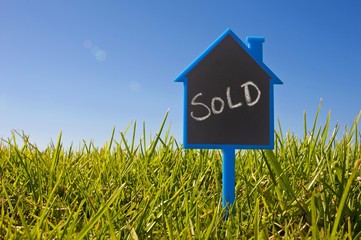 Sign shaped like a house in the grass, lettering 