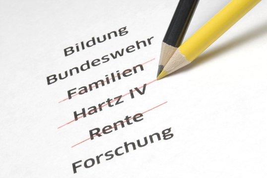 A yellow and a black pencil crossing out the letterings "Familien", "Hartz IV" and "Rente", German for "families", "Hartz IV", a German unemployment benefit, and "pension", symbolic image for the policy of economy measures of the Conservative Parties in Germany